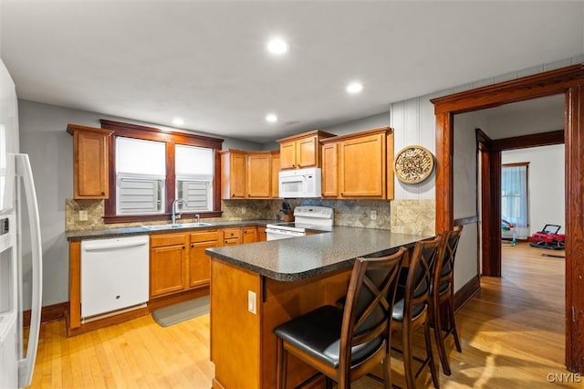 606 Tompkins St, Syracuse, NY 13204 - kitchen featuring white appliances, light wood-type flooring, decorative backsplash, brown cabinets, and dark countertops
