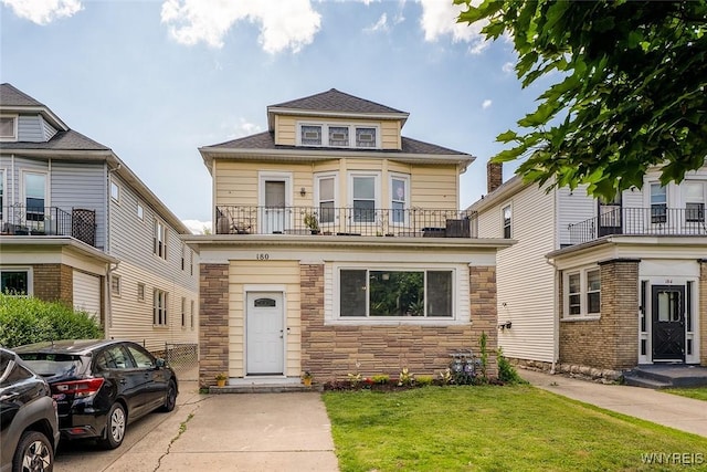 180 Lovering Ave, Buffalo, NY 14216 - american foursquare style home featuring stone siding, a front lawn, a balcony, and roof with shingles