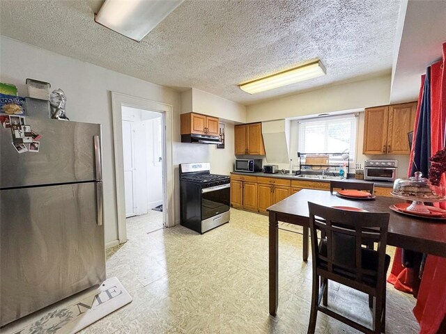 149 Post Ave, Rochester, NY 14619 - kitchen featuring stainless steel appliances, under cabinet range hood, brown cabinets, light flooring, and a textured ceiling