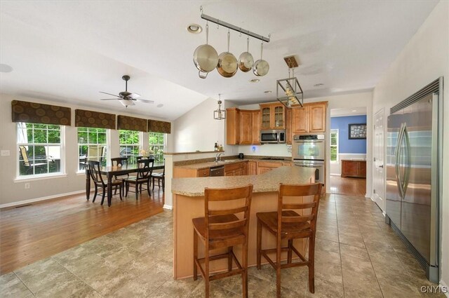 8278 Luchsinger Ln, Lysander, NY 13027 - kitchen with stainless steel appliances, a peninsula, glass insert cabinets, brown cabinets, and a ceiling fan