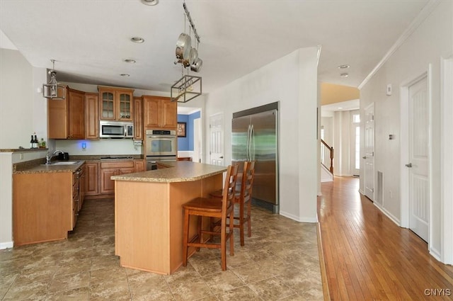 8278 Luchsinger Ln, Lysander, NY 13027 - kitchen featuring stainless steel appliances, a center island, a breakfast bar area, brown cabinetry, and glass insert cabinets
