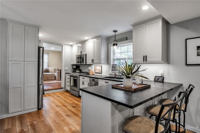17 E Ave, Leroy, NY 14482 - kitchen with stainless steel appliances, dark countertops, a peninsula, light wood-style floors, and a kitchen breakfast bar