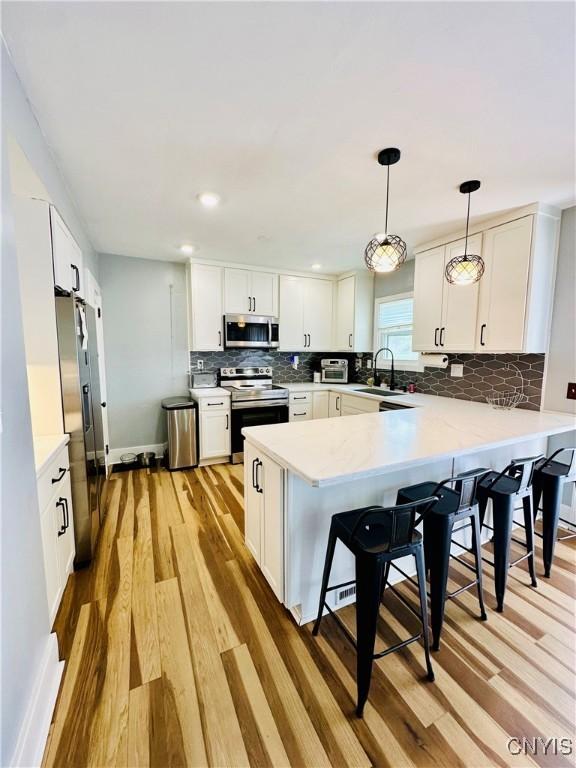 300 Hillsdale Ave, Syracuse, NY 13206 - kitchen featuring stainless steel appliances, a peninsula, light wood-type flooring, tasteful backsplash, and a kitchen bar