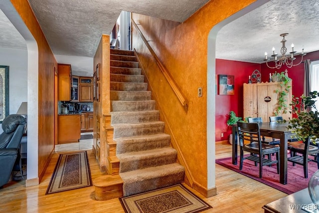 8652 Griffon Ave, Niagara Falls, NY 14304 - stairway featuring a textured ceiling, wood finished floors, arched walkways, and a chandelier