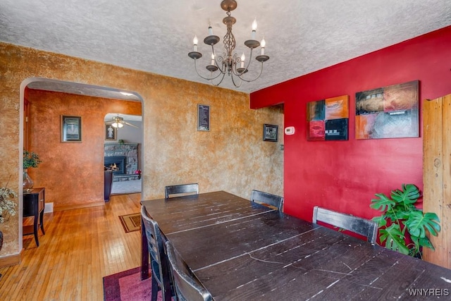 8652 Griffon Ave, Niagara Falls, NY 14304 - dining room featuring wood-type flooring, arched walkways, a chandelier, a textured ceiling, and a stone fireplace