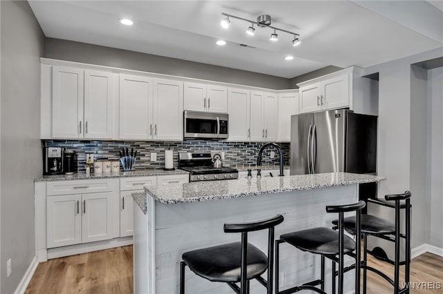 184 14th St, Buffalo, NY 14213 - kitchen featuring appliances with stainless steel finishes, white cabinets, tasteful backsplash, light wood finished floors, and a kitchen breakfast bar
