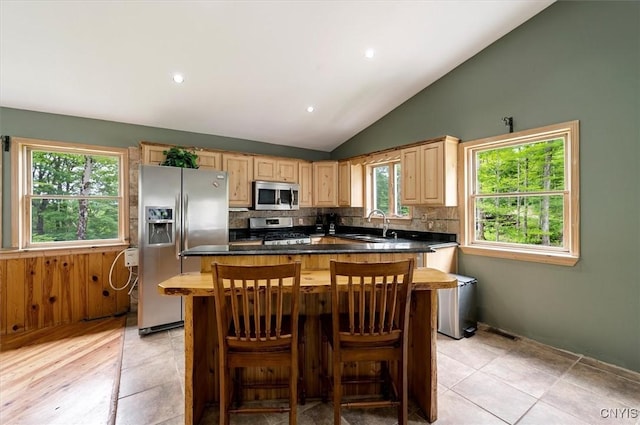 146 Mohawk Dr W, Webb, NY 13420 - kitchen featuring stainless steel appliances, light brown cabinetry, vaulted ceiling, decorative backsplash, and a kitchen island