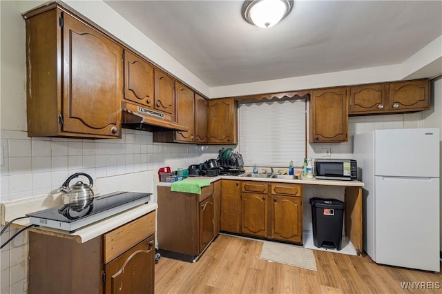 1004 19th St, Niagara Falls, NY 14301 - kitchen with freestanding refrigerator, under cabinet range hood, stainless steel microwave, light wood-style flooring, and decorative backsplash