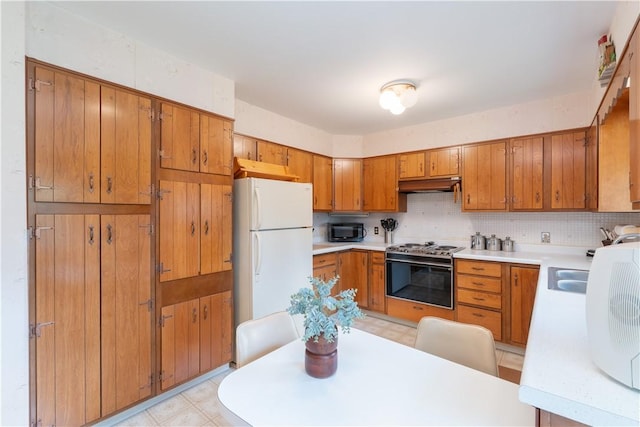 6 Meadowbrook Ter, North Dansville, NY 14437 - kitchen featuring stove, under cabinet range hood, freestanding refrigerator, black microwave, and brown cabinets