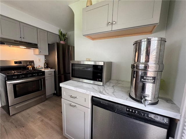 714 Arnett Blvd, Rochester, NY 14619 - kitchen featuring appliances with stainless steel finishes, under cabinet range hood, wood finished floors, light stone counters, and gray cabinetry