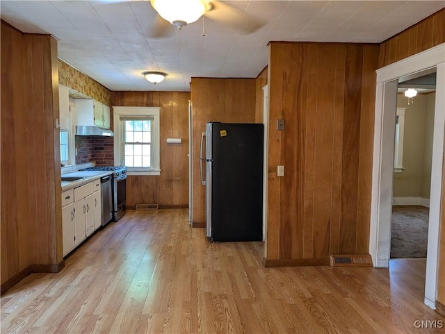 305 S Midler Ave, Syracuse, NY 13206 - kitchen with appliances with stainless steel finishes, light wood-style flooring, wooden walls, under cabinet range hood, and light countertops