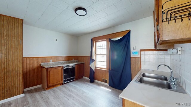 133 Freund St, Buffalo, NY 14215 - kitchen featuring black dishwasher, a wainscoted wall, brown cabinetry, light wood-style flooring, and wooden walls