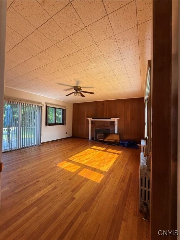 5877 State Route 233, Westmoreland, NY 13440 - unfurnished living room featuring ceiling fan, wood walls, wood finished floors, and a fireplace