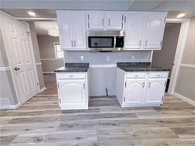 221 82nd St, Niagara Falls, NY 14304 - kitchen with stainless steel microwave, light wood-style flooring, dark countertops, white cabinetry, and recessed lighting