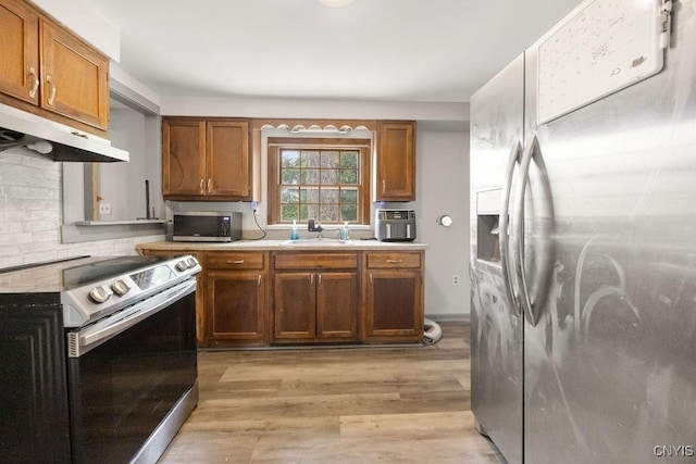 9 Lawrence Ave, New Hartford, NY 13413 - kitchen featuring appliances with stainless steel finishes, light countertops, light wood-style floors, brown cabinetry, and under cabinet range hood