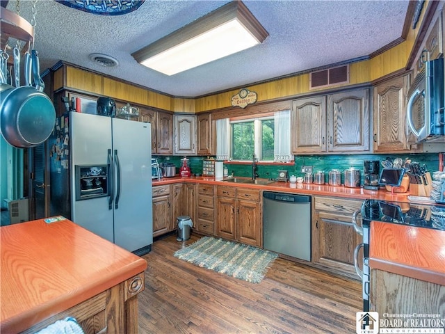 5152 John Darling Rd, Conowingo, NY 14726 - kitchen featuring appliances with stainless steel finishes, a textured ceiling, dark wood-style flooring, tasteful backsplash, and brown cabinets