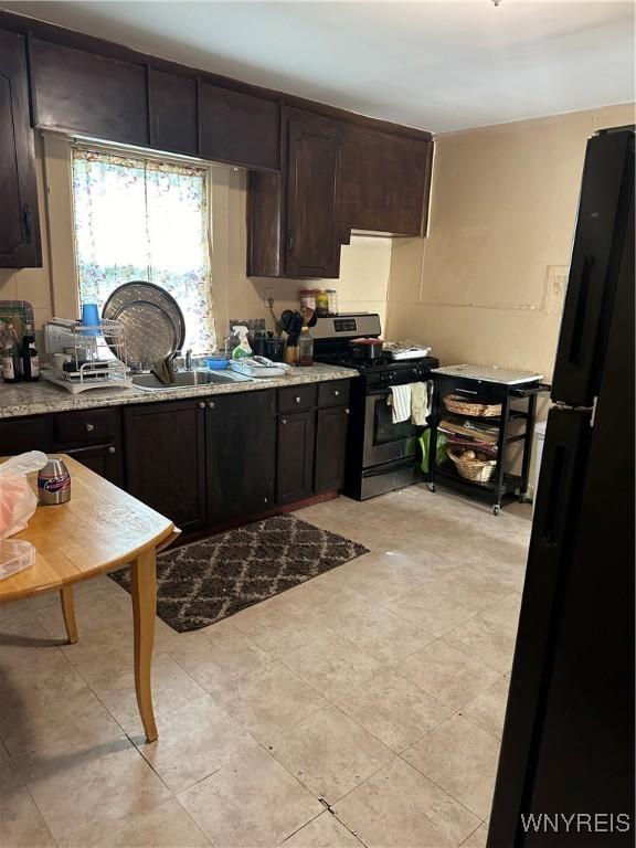 54 Decker St, Buffalo, NY 14215 - kitchen featuring stainless steel gas range, freestanding refrigerator, dark brown cabinets, and light tile patterned flooring