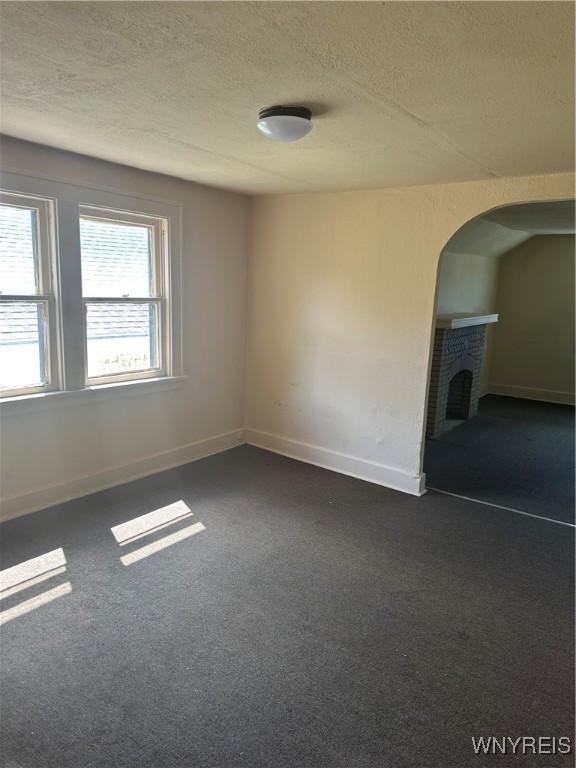 54 Decker St, Buffalo, NY 14215 - spare room with a textured ceiling, arched walkways, dark carpet, and a fireplace