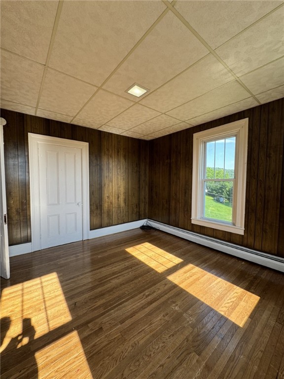 2 2nd St, Eldred, PA 16731 - unfurnished room with a baseboard radiator, wood finished floors, a paneled ceiling, and wood walls