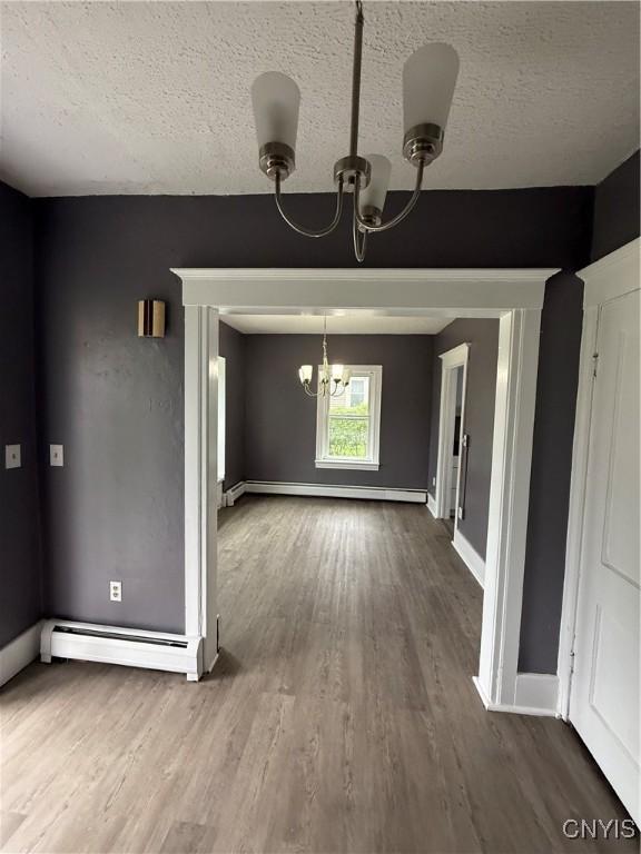 37 Peacock St, Auburn, NY 13021 - unfurnished dining area with a chandelier, a baseboard heating unit, wood finished floors, a textured ceiling, and baseboard heating