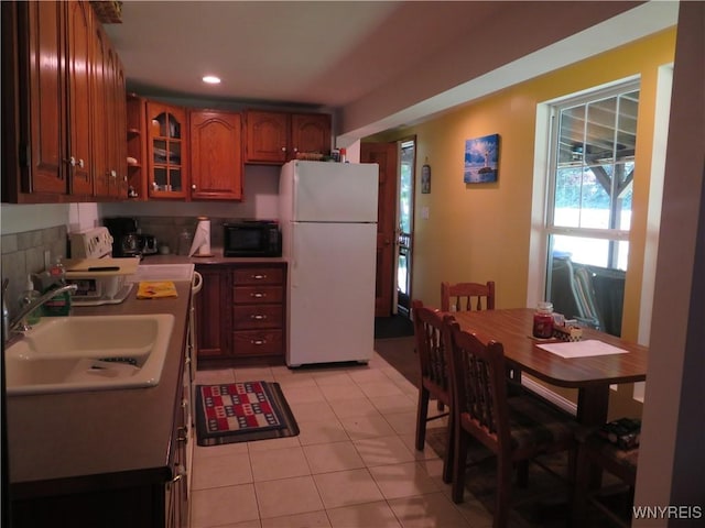 8211 Elmwood Dr, Rushford, NY 14717 - kitchen featuring freestanding refrigerator, black microwave, light tile patterned floors, glass insert cabinets, and brown cabinetry