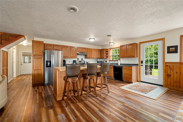224 Macarthur Rd, Russia, NY 13324 - kitchen with appliances with stainless steel finishes, dark wood finished floors, a kitchen island, a textured ceiling, and a breakfast bar area