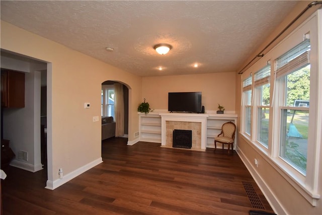 166 Burwell Rd, Irondequoit, NY 14617 - unfurnished living room featuring a textured ceiling, arched walkways, plenty of natural light, wood finished floors, and a tiled fireplace