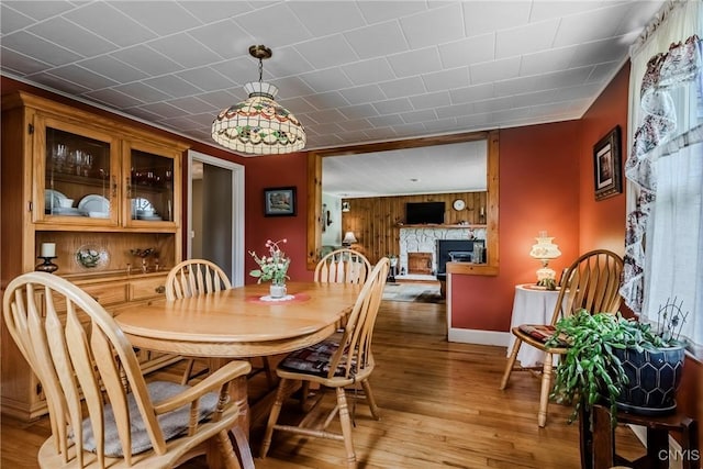 6954 Rome Oriskany Rd, Rome, NY 13440 - dining area with light wood-type flooring, wood walls, and a fireplace with raised hearth