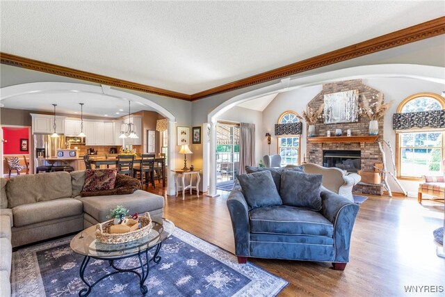 5477 Pebble Beach Dr, Hamburg, NY 14075 - living area featuring arched walkways, a brick fireplace, wood finished floors, a textured ceiling, and vaulted ceiling