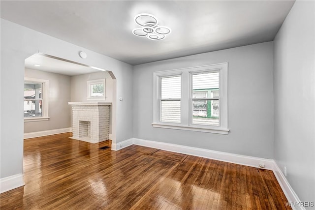 717 Lasalle Ave, Buffalo, NY 14215 - unfurnished living room featuring wood finished floors, arched walkways, and a brick fireplace