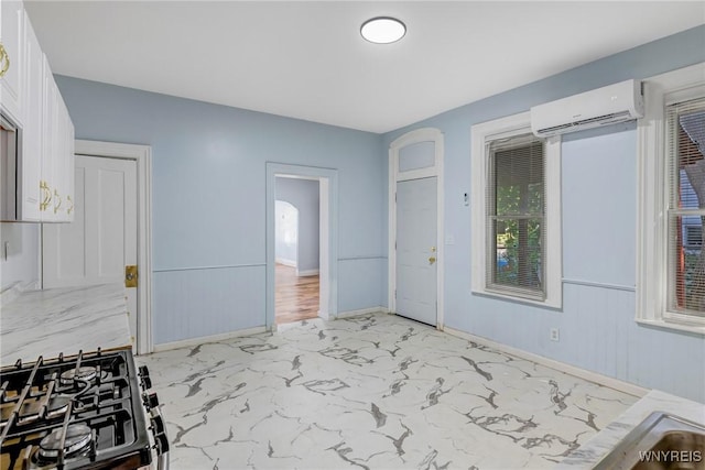 152 Mulberry St, Buffalo, NY 14204 - kitchen with a wall mounted AC, light marble finish floors, gas range oven, white cabinetry, and light countertops