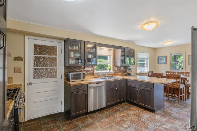 4853 Enders Rd, Manlius, NY 13104 - kitchen with stainless steel appliances, a peninsula, dark brown cabinetry, glass insert cabinets, and backsplash