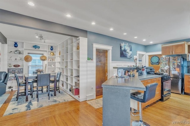 592 Parkside Ave, Buffalo, NY 14216 - kitchen with black range with gas cooktop, freestanding refrigerator, light wood-type flooring, a breakfast bar, and wainscoting