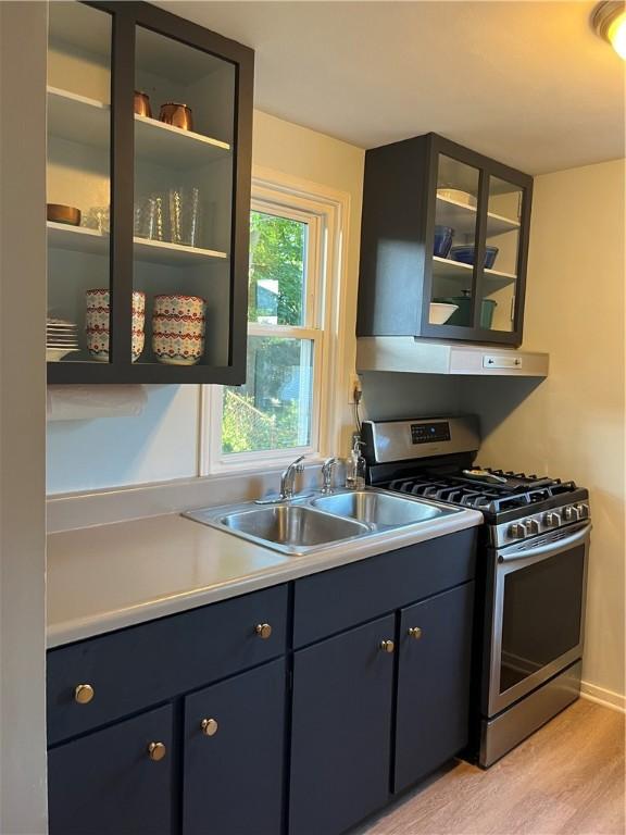 584 Falstaff Rd, Irondequoit, NY 14609 - kitchen featuring gas stove, wall chimney exhaust hood, light countertops, light wood finished floors, and glass insert cabinets