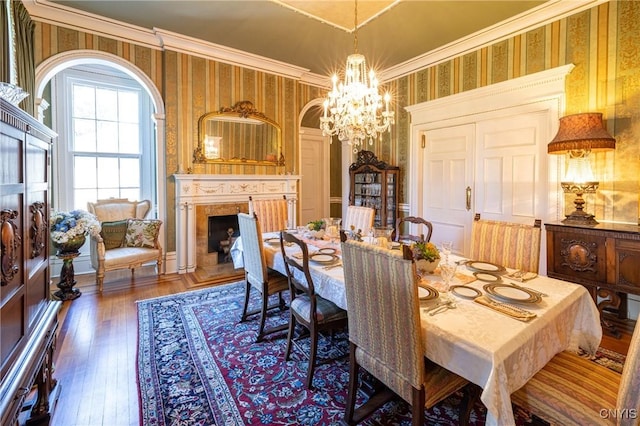 71 Forman St, Cazenovia, NY 13035 - dining space with wallpapered walls, a chandelier, a fireplace, wood-type flooring, and crown molding