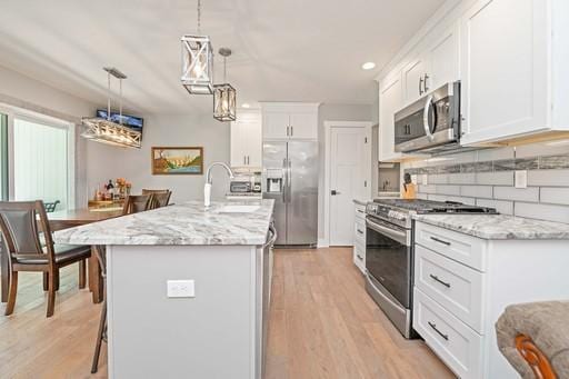 61 Kirkdale Cir, Greece, NY 14612 - kitchen featuring stainless steel appliances, white cabinets, a center island with sink, light wood-style floors, and light stone countertops