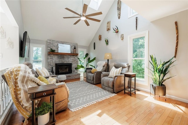 346 Willowood Dr, Greece, NY 14612 - living room featuring a brick fireplace, hardwood / wood-style flooring, high vaulted ceiling, a ceiling fan, and a skylight