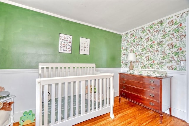 103 Culver Pkwy, Irondequoit, NY 14609 - bedroom featuring wallpapered walls, ornamental molding, a wainscoted wall, wood finished floors, and a crib