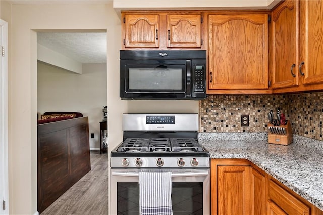 73 Hazel Bark Run, Gates, NY 14606 - kitchen with black microwave, gas range, decorative backsplash, light stone counters, and brown cabinets