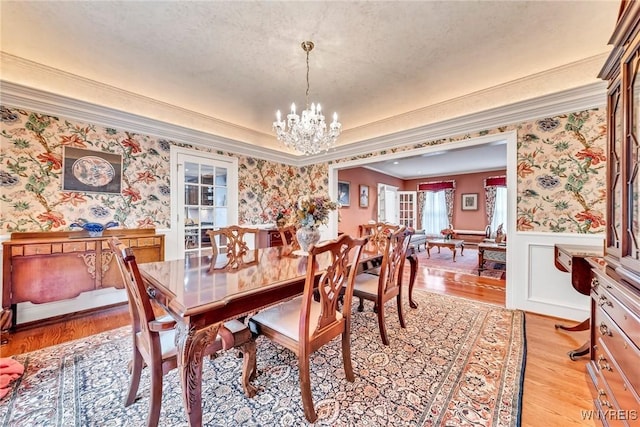 9555 The Maples, Clarence, NY 14031 - dining room featuring wallpapered walls, a chandelier, a wainscoted wall, light wood-type flooring, and crown molding
