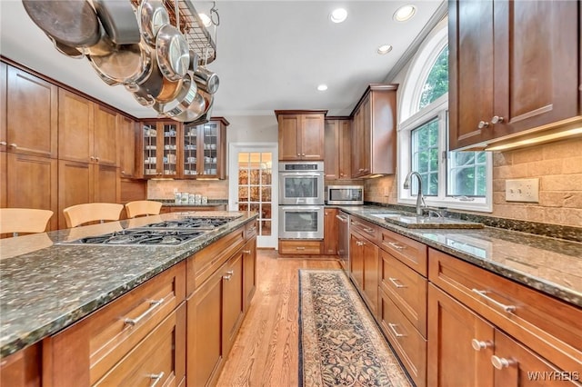 9555 The Maples, Clarence, NY 14031 - kitchen featuring appliances with stainless steel finishes, crown molding, light wood-style flooring, brown cabinetry, and dark stone counters