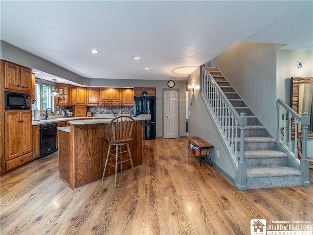 5616 Stow Rd, North Harmony, NY 14710 - kitchen featuring black appliances, brown cabinetry, a kitchen island, light wood finished floors, and a kitchen bar