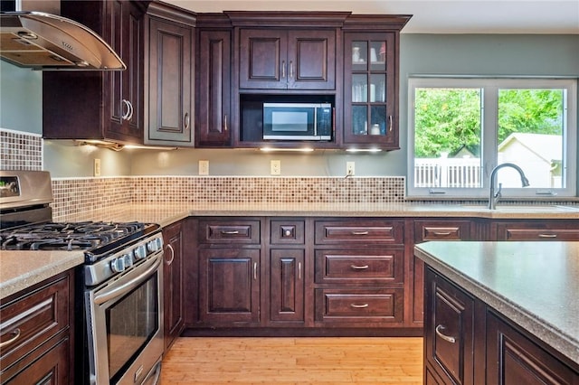 184 Main St, Phelps, NY 14532 - kitchen with stainless steel gas range oven, exhaust hood, light wood-style flooring, glass insert cabinets, and light countertops