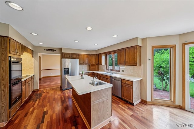 100 Hunt Club Cir, Amherst, NY 14051 - kitchen featuring appliances with stainless steel finishes, light countertops, wood finished floors, decorative backsplash, and a center island with sink