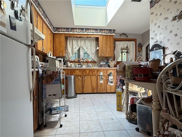 3902 Calkins Rd, Porter, NY 14174 - kitchen featuring freestanding refrigerator, brown cabinetry, wallpapered walls, and a skylight