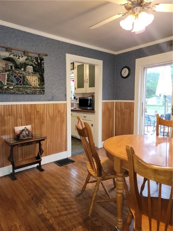 244 State Highway 320, Norwich, NY 13815 - dining space with a wainscoted wall, wood finished floors, ornamental molding, a ceiling fan, and wooden walls
