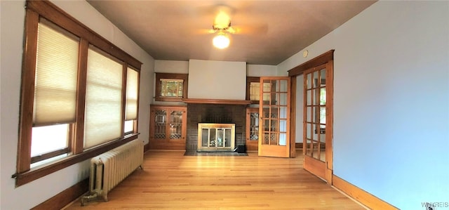 425 12th St, Niagara Falls, NY 14303 - unfurnished living room featuring radiator, a fireplace, light wood finished floors, and ceiling fan
