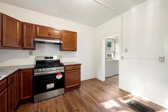 117 Prospect St, Lenox, NY 13032 - kitchen with stainless steel gas range oven, under cabinet range hood, washer / clothes dryer, wood finished floors, and brown cabinetry