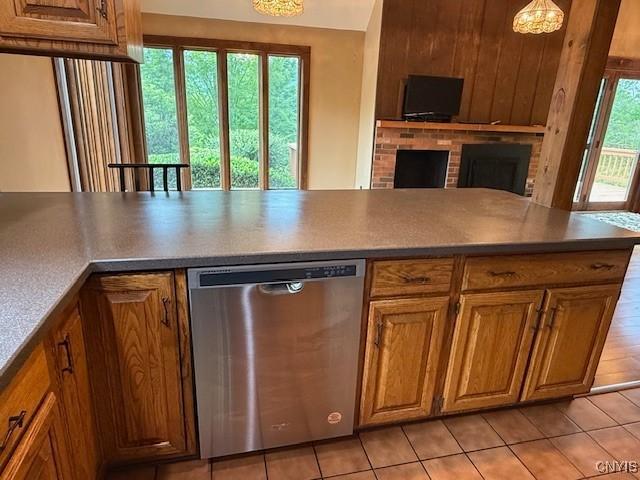 2033 Artemis Dr, Virgil, NY 13045 - kitchen with stainless steel dishwasher, a brick fireplace, light tile patterned flooring, and brown cabinetry