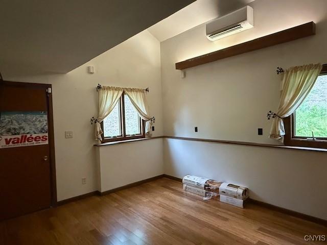 2033 Artemis Dr, Virgil, NY 13045 - empty room featuring an AC wall unit, wood finished floors, and vaulted ceiling